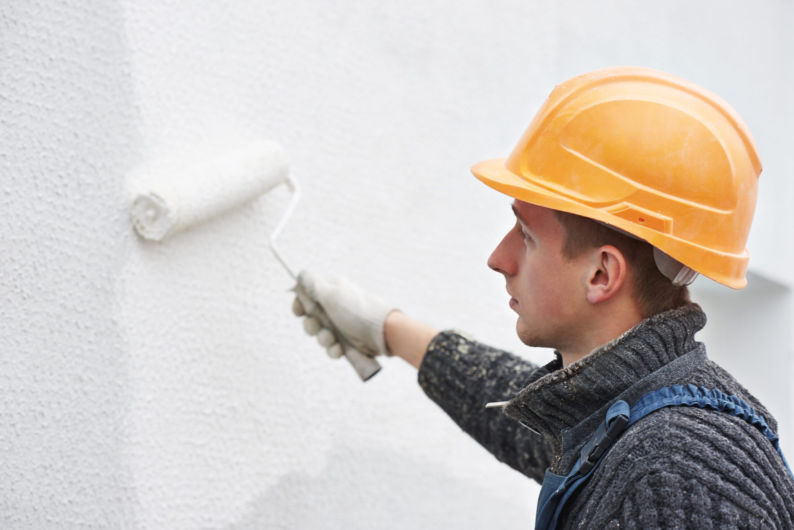 builder worker painting facade of high-rise building with roller